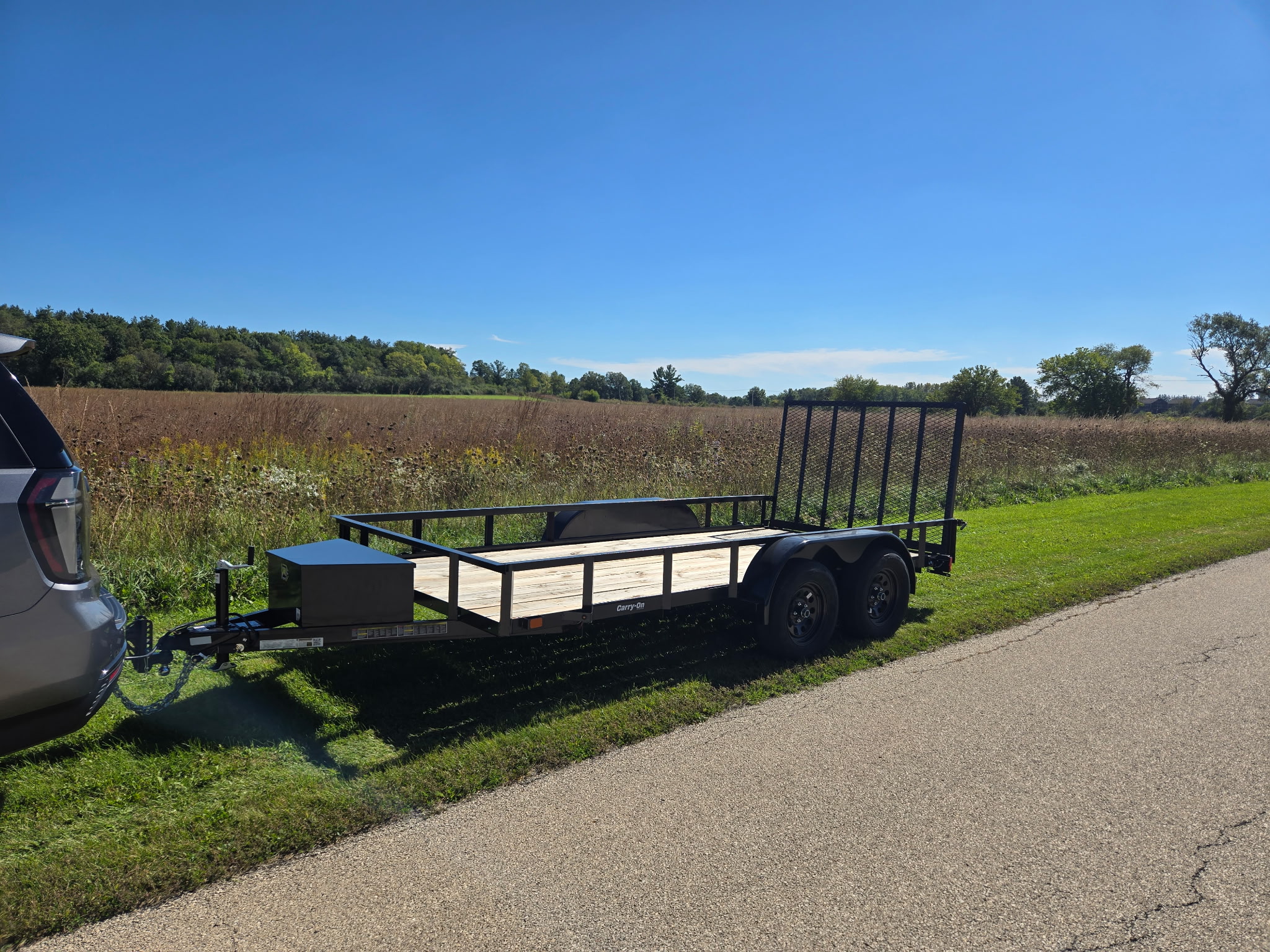 Side view of the tandem-axle utility trailer hitched to an SUV on a country road, ramp gate up