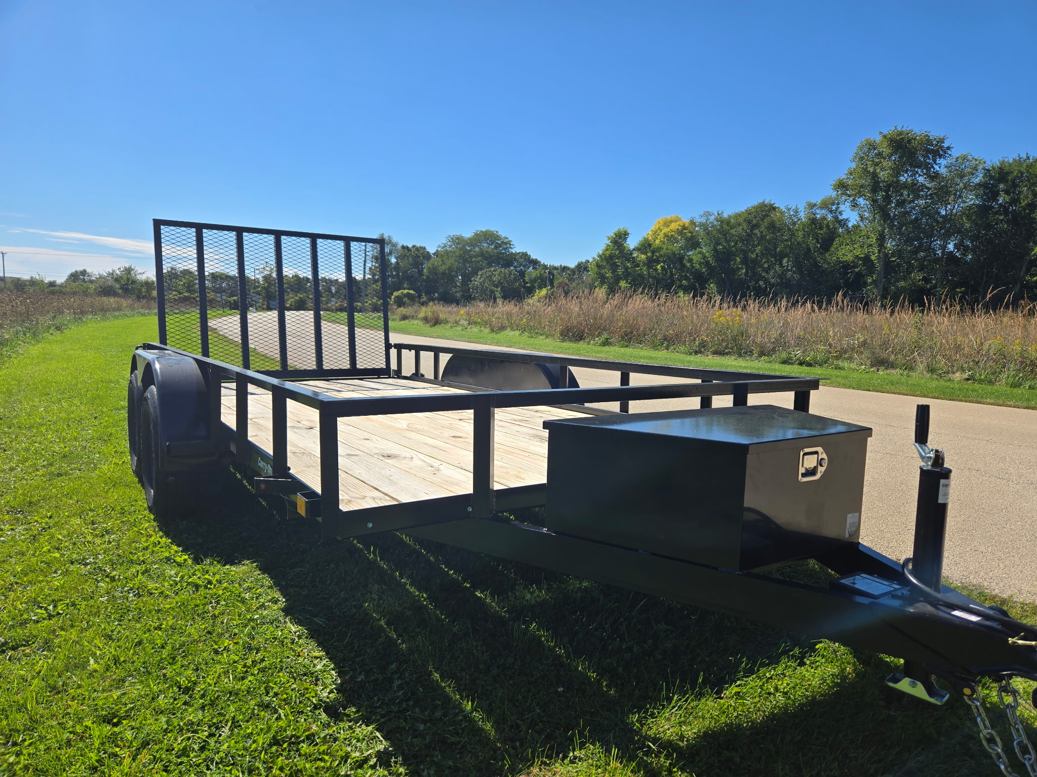 Front three-quarter view of the trailer showing the tongue toolbox, jack and raised ramp gate
