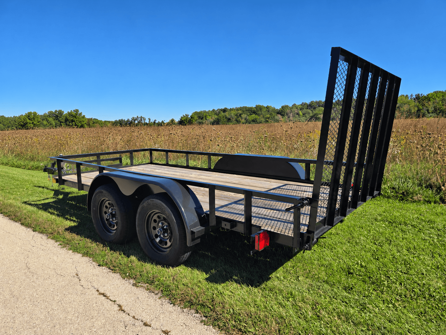 Hook & Haul tandem-axle utility trailer with its ramp gate up, parked on grass beside a prairie