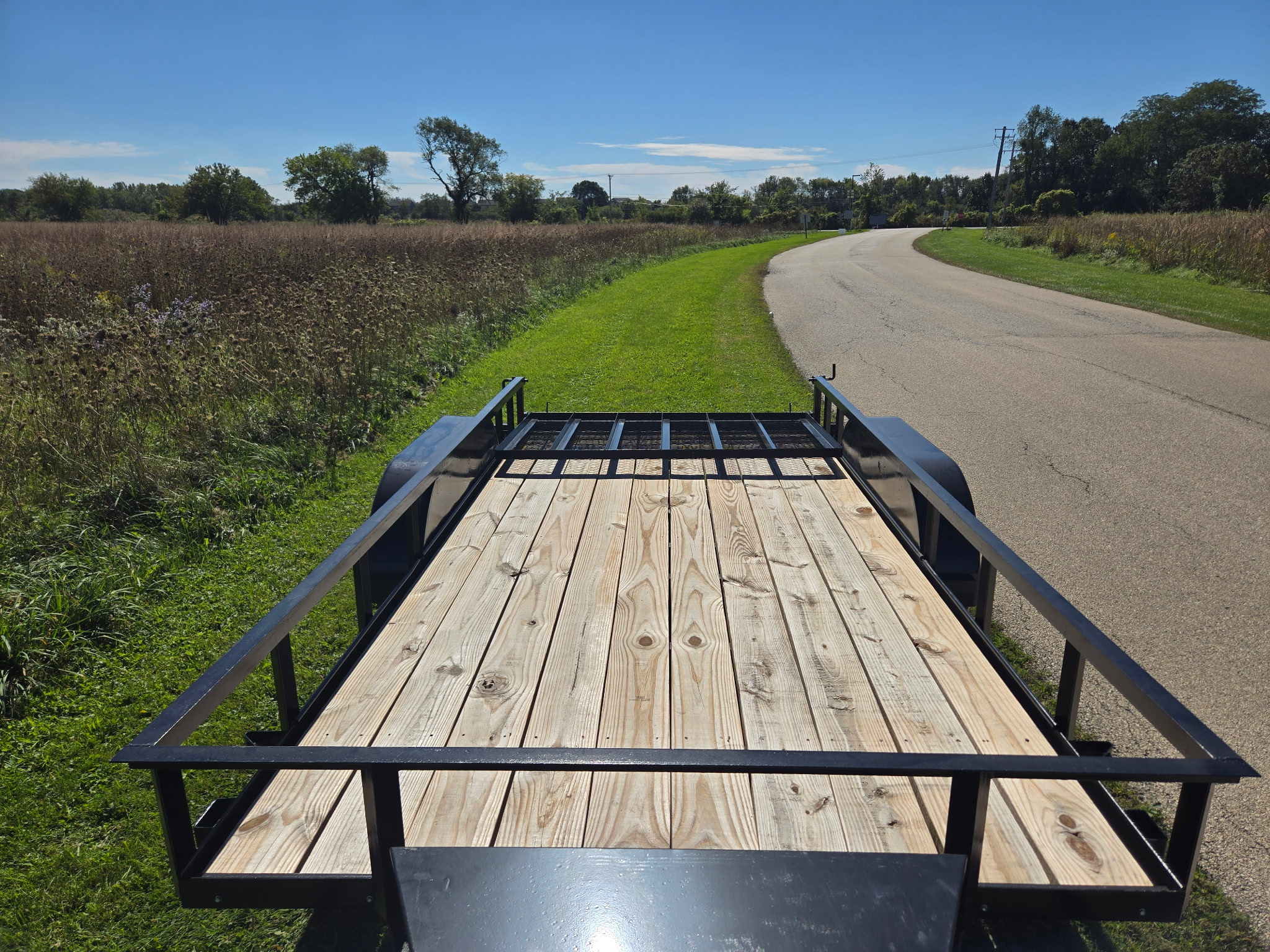 Wood deck and rails of the Hook & Haul utility trailer, parked along a country road beside a prairie